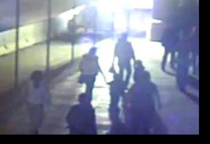 (Image 7) Border-crossing video. A group of four, from behind — an adult male, an adult female in a light coat, a light-colored bag, and two children — crossing into Mexico.