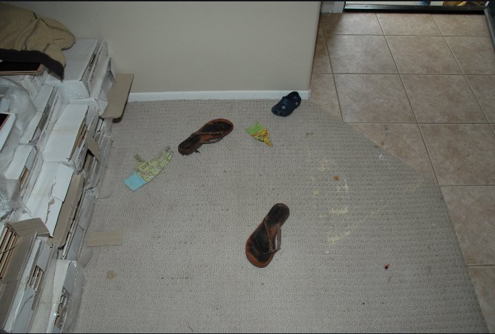 Trial Exhibit 29 — interior of the residence: two sandals and children's items on the carpet near the tiled entry, with a pale stain visible on the carpet